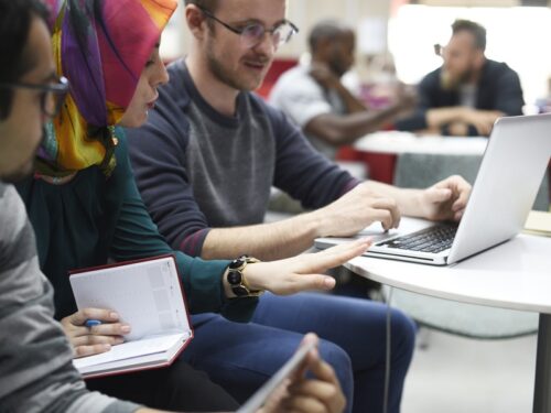 Three people are sat together discussing an exercise in an AI Adoption workshop and viewing a laptop together.